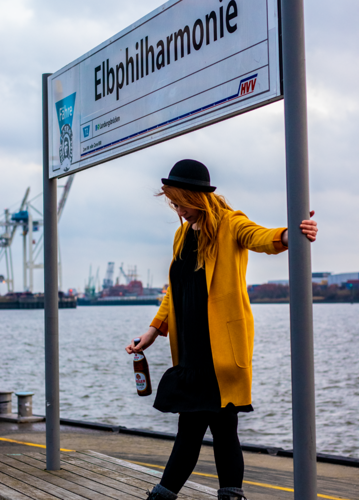 Christina Schwärzler steht mit einem Kölsch Bier an der Hamburger Haltestelle Elbphilharmonie