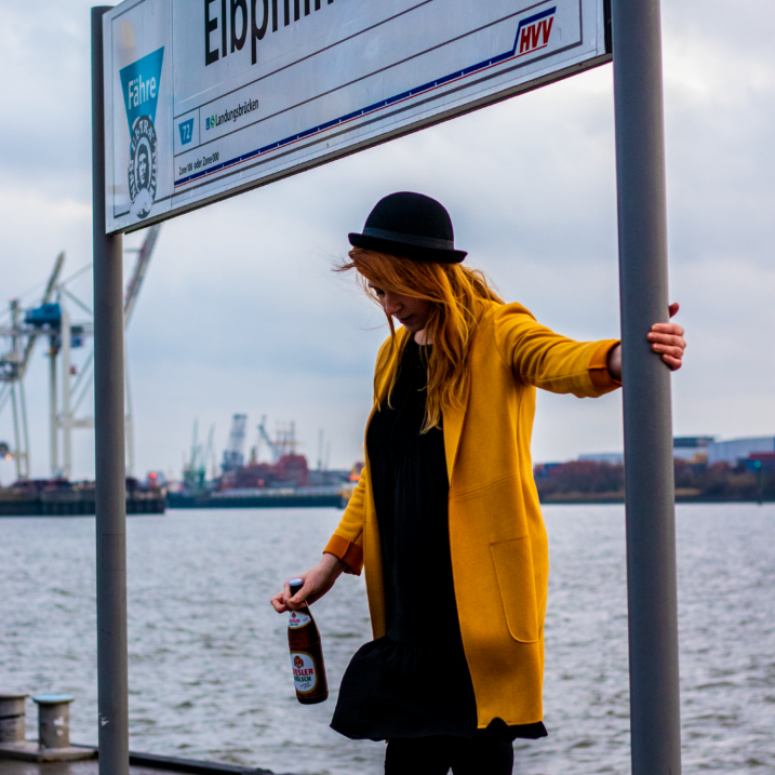 Christina Schwärzler steht mit einem Kölsch Bier an der Hamburger Haltestelle Elbphilharmonie